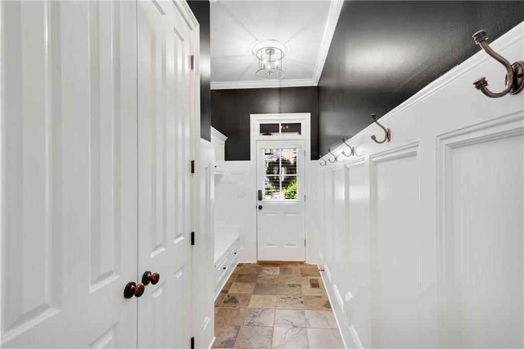 Formal dining room at 3075 Wills Mill: long wood table with white slipcovered chairs, beaded chandelier, dark accent walls, white wainscoting, tall sheer-curtained windows looking onto the front yard, upright piano in the foreground